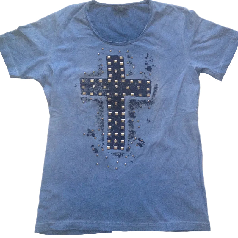 A blue short-sleeve t-shirt laid flat on a white fabric background, featuring a large distressed cross graphic on the front with a grid pattern and small metallic studs.