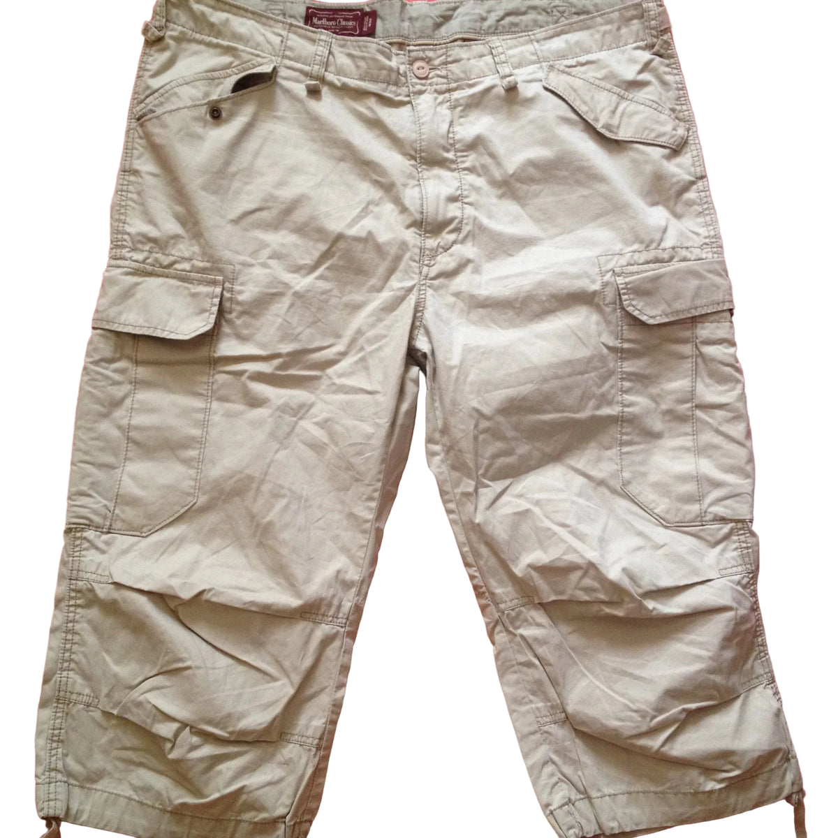 A pair of beige cargo shorts with multiple flap pockets, laid flat on a red fabric background.