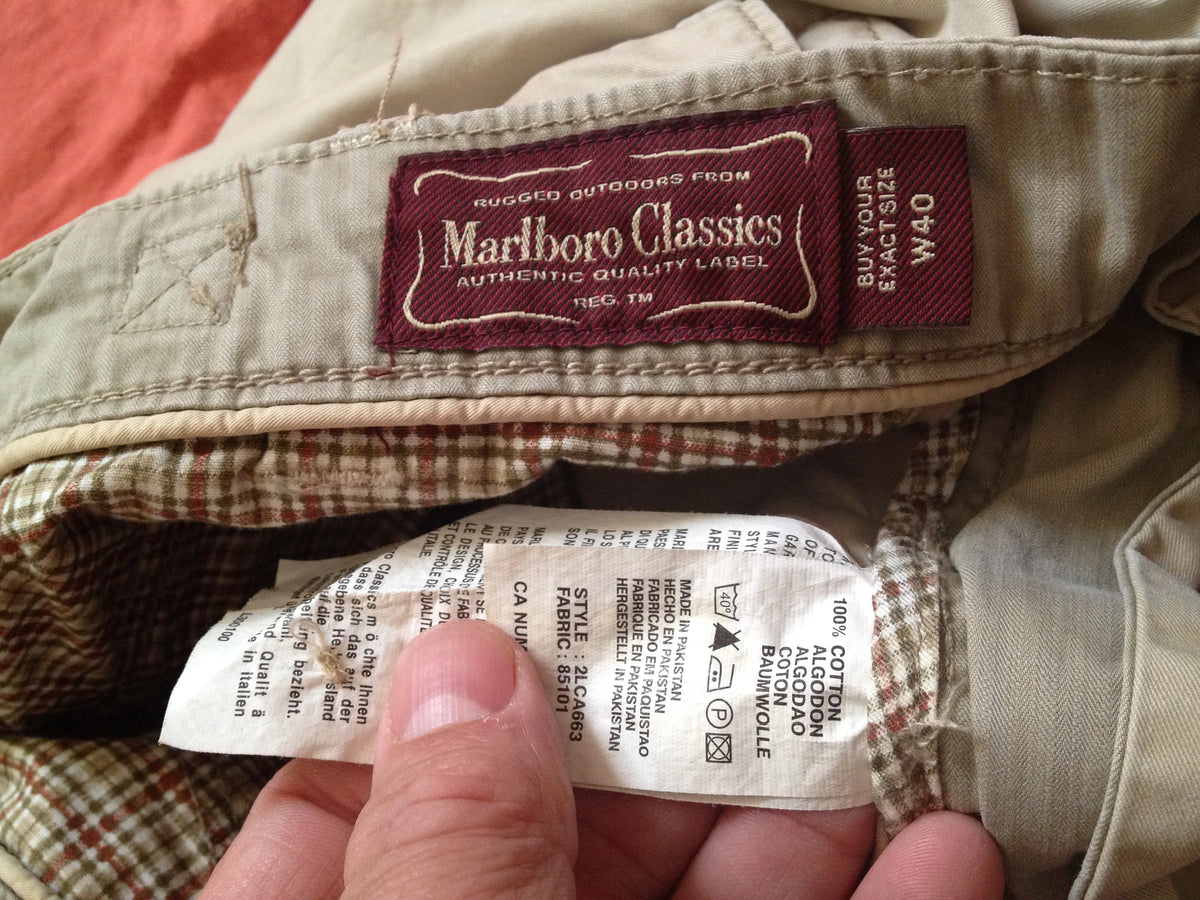 Close-up of a vintage pair of Marlboro Classics jeans showing the interior waistband, a sewn-on brand label, and a hand holding the inside care tag.
