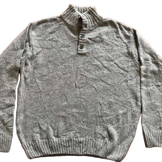 A gray heathered knit sweater with a mock neck and button placket, laid flat on a red fabric background.